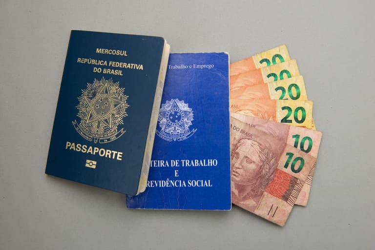 Passaporte, carteira de trabalho e cédulas de dinheiro em uma superfície cinza.
