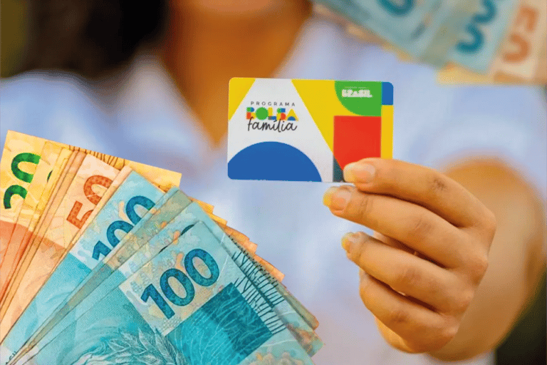 Cartão do programa Bolsa Família sendo exibido com cédulas de reais ao fundo.