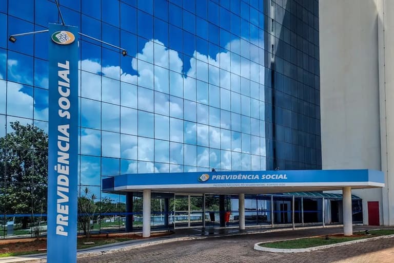 Fachada moderna do edifício da Previdência Social refletindo o céu azul com nuvens.