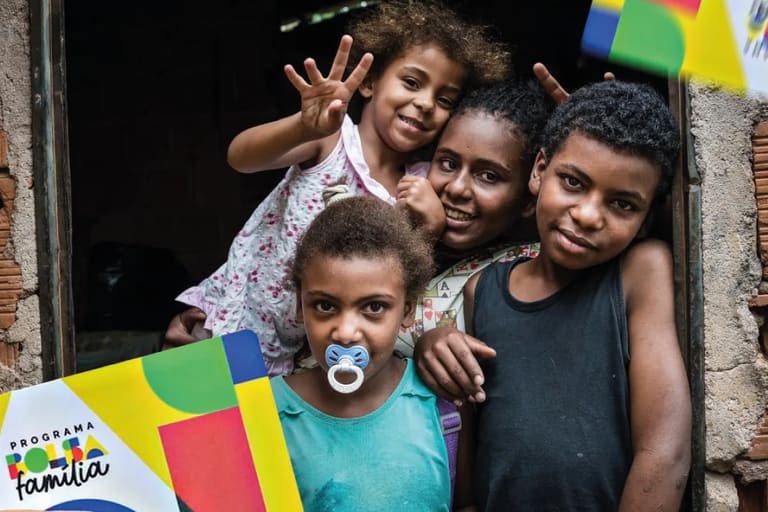 Família sorrindo na porta de casa representando os beneficiários do Bolsa Família