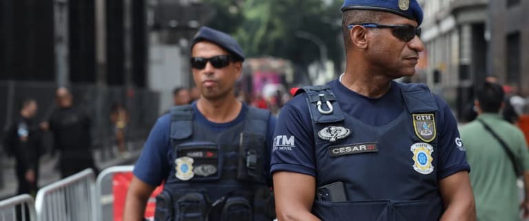 Dois membros da Guarda Municipal de Rio de Janeiro em patrulhamento, com uniformes de segurança e fardamento tático, durante ação na cidade.