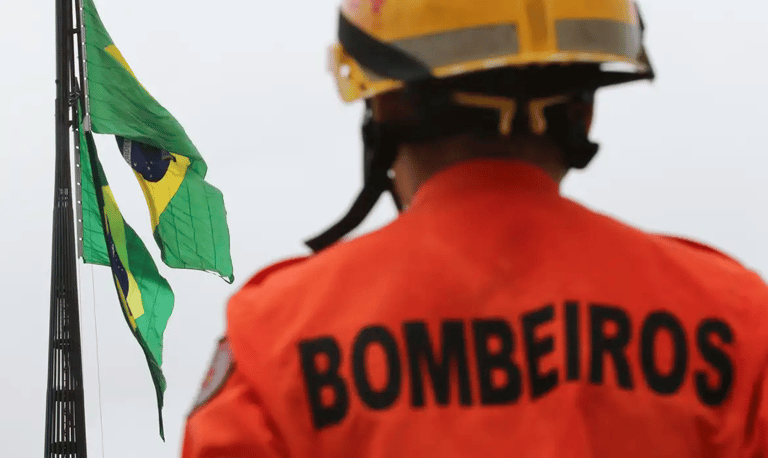 Bombeiro de costas com a palavra BOMBEIROS estampada no uniforme laranja.