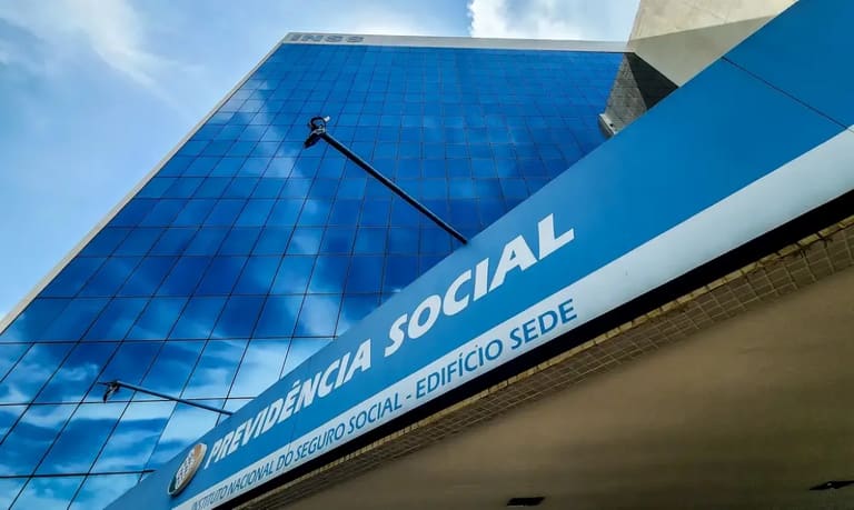 INSS anuncia pagamentos a partir de R$ 1.518 em agosto Imagem da sede do INSS, com a fachada visível, em azul e branco, anunciando informações sobre os pagamentos de agosto.