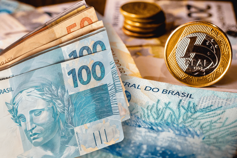 Cédulas e moedas de Real, representando o benefício financeiro de R$ 1.050 que será pago por meio de PIX.