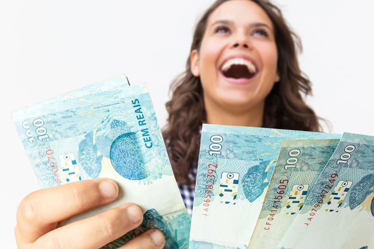 Pessoa sorrindo e segurando notas de 100 reais, simbolizando conquistas financeiras e bons negócios.