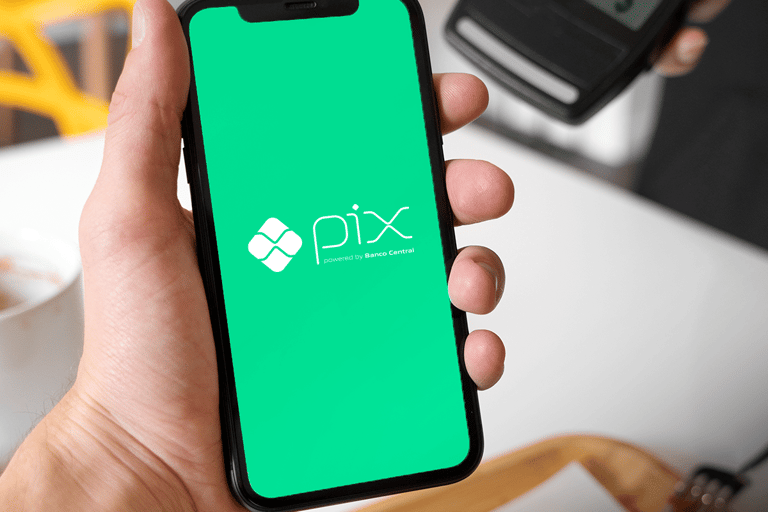 Pix parcelado Mão segurando smartphone com tela do Pix e maquinininha ao fundo