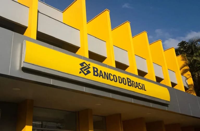 Fachada do Banco do Brasil, com a logo amarela e azul, em uma imagem representando o tema do concurso e a exigência de um novo edital pelo sindicato.