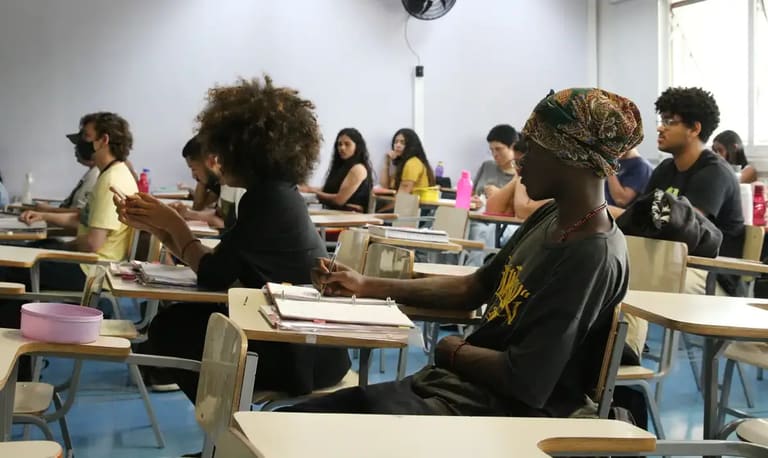 Cursos Técnicos Estudantes atentos em sala de aula, com alguns usando máscaras e outros com garrafas de água.
