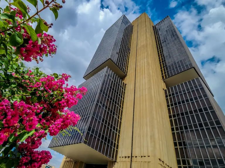 Edifício do Banco Central do Brasil em Brasília, com flores cor-de-rosa em primeiro plano, ilustrando a nova política de restrição de transferências para contas suspeitas de atividades ilícitas.