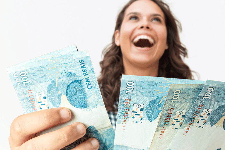 Mulher sorridente segurando notas de 100 reais comemorando aumento salarial