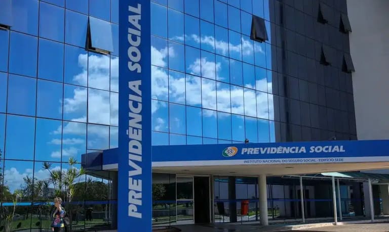 Imagem do prédio do INSS com fachada em vidro refletindo o céu, associado à revisão de benefícios.