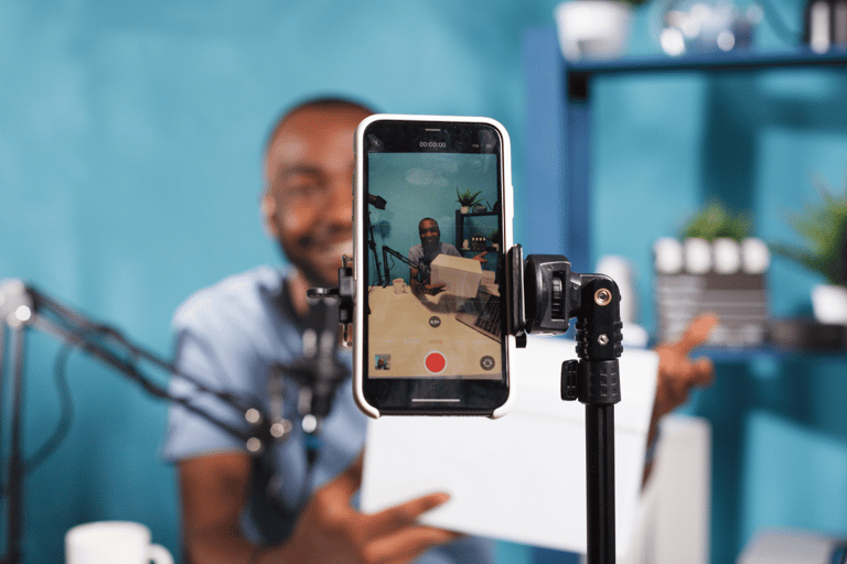 Homem gravando vídeo com smartphone em tripé para criação de conteúdo digital.