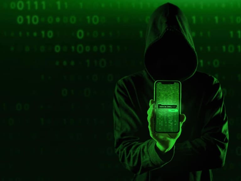 Figura encapuzada segurando smartphone com código verde matrix na tela representando cibercriminoso aplicando golpe