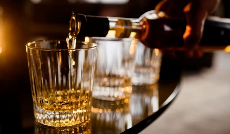 Homem servindo bebida alcoólica em copos, com foco na ação de despejar o líquido dourado.