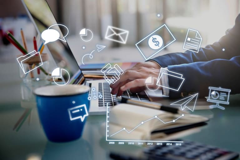Pessoa trabalhando em um notebook com diversos ícones digitais e de negócios (mensagens, e-mail, dinheiro, gráficos) flutuando ao redor, representando as mudanças e inovações nas profissões de Saúde, Logística e Marketing Digital.