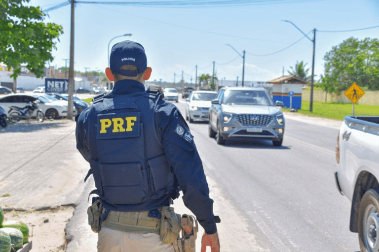 Agente da Polícia Rodoviária Federal vistoriando veículos em movimentada estrada durante o dia