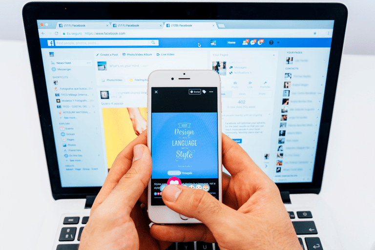 Pessoa segurando smartphone mostrando postagem no Facebook com laptop ao fundo exibindo a rede social.