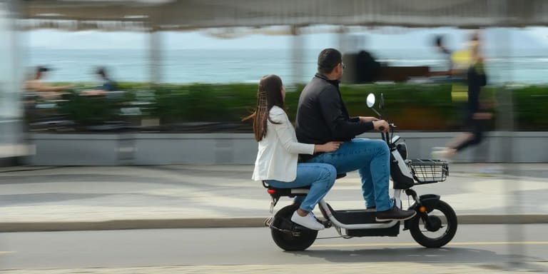 Homem e mulher pilotando juntos uma moto elétrica preta e branca em uma avenida urbana