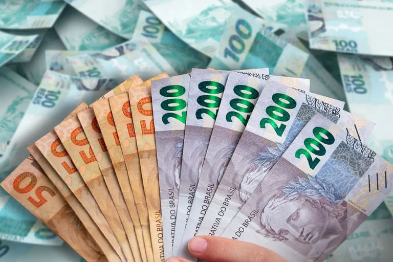 Mão de uma pessoa segurando notas de R$ 100 reais, simbolizando o reajuste do Salário Mínimo que entrará em vigor em 2026.