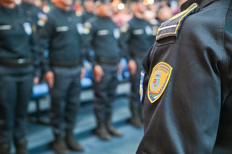 Guarda Municipal em formação, com uniforme preto e brasão da corporação em destaque no ombro.