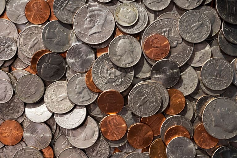 Visão aérea de diversas moedas americanas antigas e modernas misturadas, incluindo moedas de Kennedy, Washington e Lincoln, ilustrando a conservação de moedas raras.
