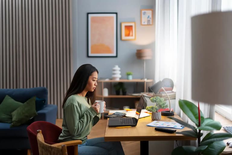 Pessoa concentrada, com uma xícara na mão, estudando em seu escritório, com laptop e materiais de estudo na mesa, ideal para ilustrar a preparação para os concursos de 2026.