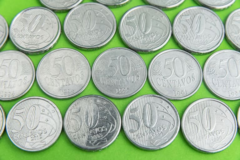Visão aproximada de uma moeda de 50 centavos de 2019 segurada por dedos, destacando a letra "A" próxima à data.