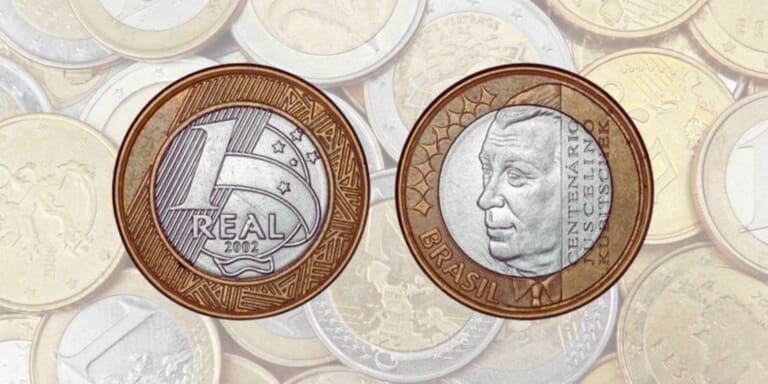 Frente e verso da moeda de 1 Real comemorativa do Centenário de Juscelino Kubitschek (2002) sobre um fundo de várias moedas desfocadas.