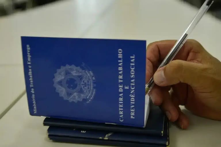 Carteira de Trabalho e Previdência Social sendo preenchida com caneta, representando o processo de solicitação do Seguro-Desemprego.