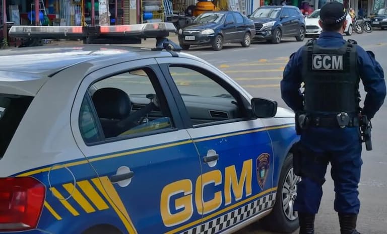 Imagem de um guarda municipal em patrulhamento ao lado de um veículo da Guarda Municipal com a inscrição 'GCM' visível.