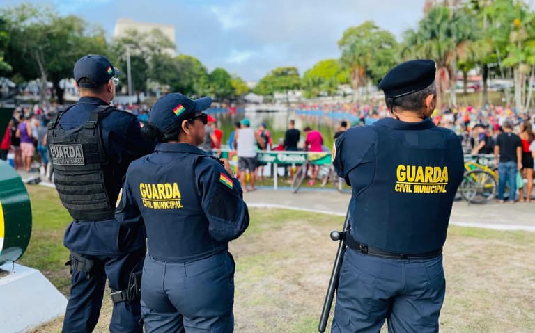Três guardas municipais vigiam evento ao ar livre com grande público e área verde