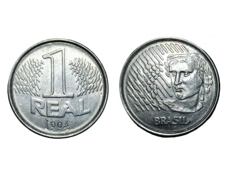 Visão detalhada das duas faces da primeira moeda de 1 real do Brasil, lançada em 1994. À esquerda, o reverso com o número 1 sobre ramos de louro; à direita, o anverso exibindo a efígie da República e a palavra "Brasil" sobre um fundo branco.