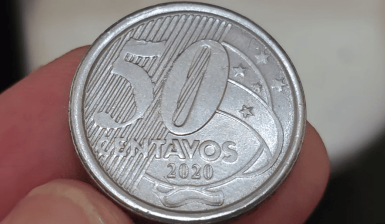Fotografia em close-up do reverso de uma moeda de 50 centavos de 2020, segurada entre os dedos. A imagem destaca o número 50, a palavra "CENTAVOS" e o ano de fabricação 2020 sobre o fundo de linhas diagonais.