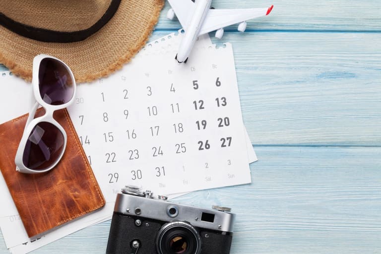 Calendário mensal com itens de viagem sobre mesa azul simbolizando a divulgação dos feriados nacionais e pontos facultativos de 2026.