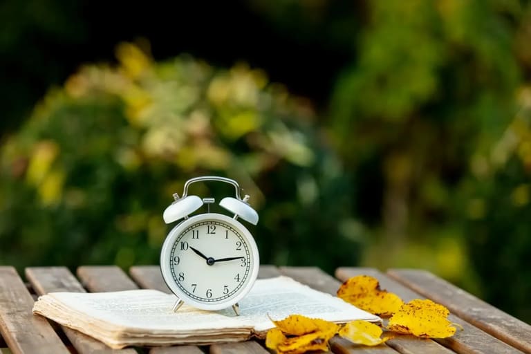 Relógio de alarme sobre livro com folhas de outono, representando o possível horário de verão 2026 no Brasil