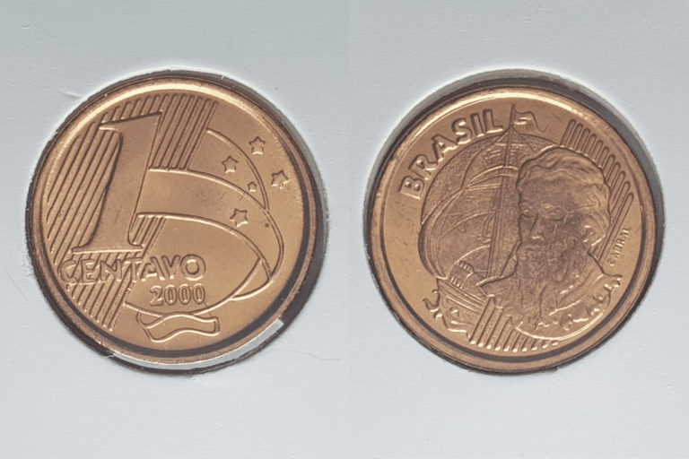 Montagem mostrando as duas faces de uma moeda de 1 centavo de 2000 em suportes brancos. À esquerda, o reverso exibe o número "1", a palavra "CENTAVO" e o ano "2000". À direita, o anverso mostra a efígie de Pedro Álvares Cabral ao lado de uma nau.