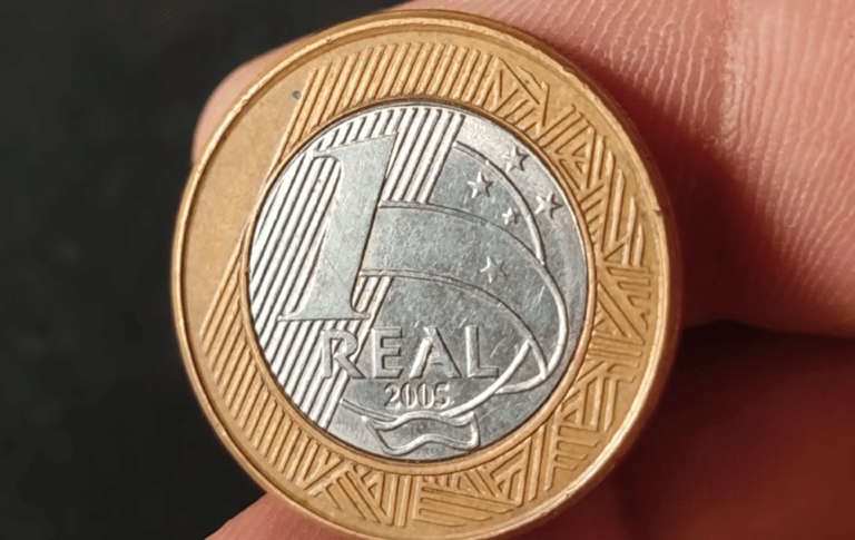 Close de uma moeda de 1 real do ano de 2005, com foco na data gravada na base dourada e no rosto da República no centro prateado.