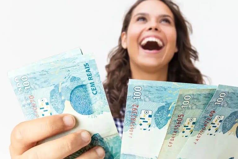 Pessoa sorrindo segurando cédulas de R$ 100,00, relacionada ao pagamento do auxílio de R$ 1.000,00 da Caixa para CPFs com finais de 0 a 9, nos dias 26 e 27 de fevereiro de 2026.