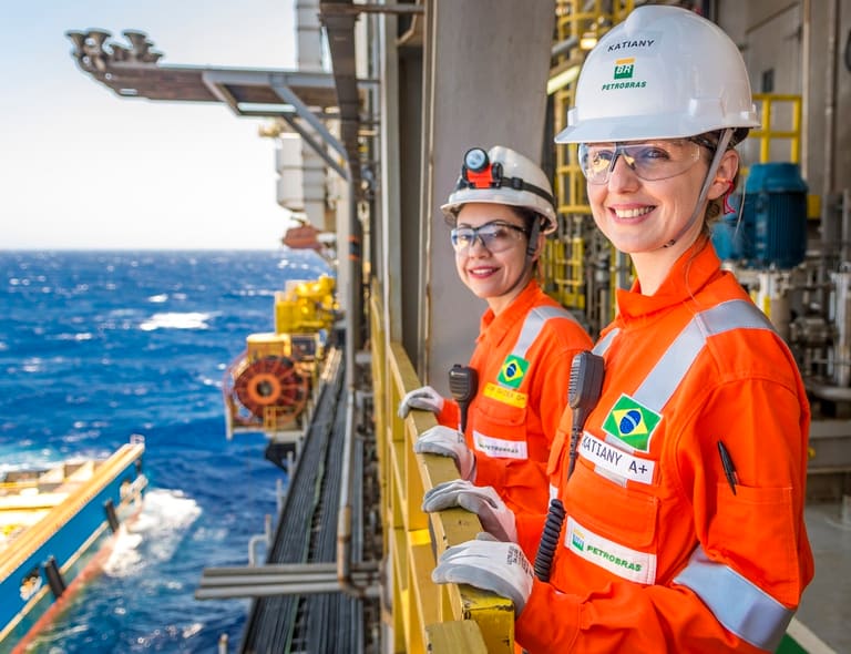 Duas funcionárias da Petrobras usando uniforme laranja e capacete em plataforma de petróleo no mar