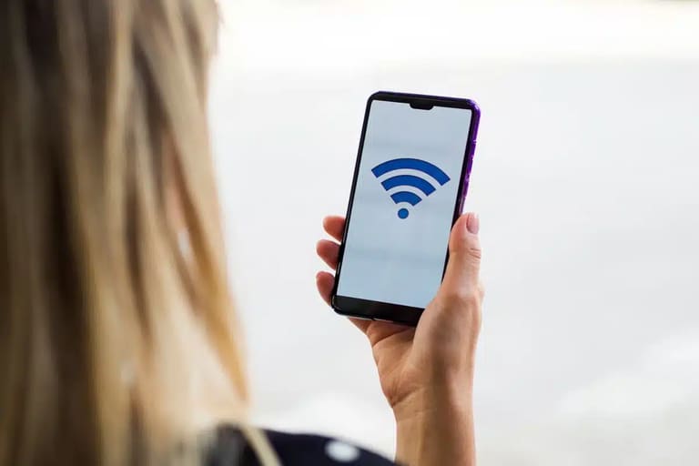 Mulher segurando smartphone com símbolo de Wi-Fi na tela, representando riscos de manter a conexão ativa o tempo todo.