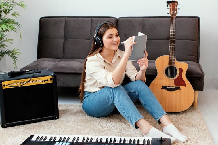 Jovem estudando inglês com música enquanto ouve fones de ouvido e faz anotações ao lado de um violão.