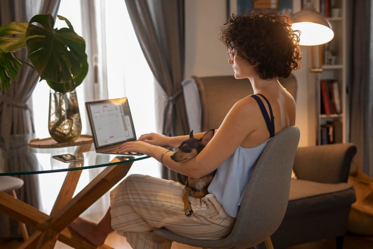 Mulher trabalhando em home office com notebook e cachorro no colo representando profissões remotas com salário acima de R$ 5 mil