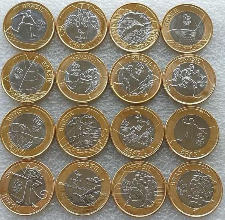 Coleção completa com 16 moedas de 1 Real comemorativas dos Jogos Olímpicos Rio 2016, exibindo diferentes modalidades esportivas e os mascotes Tom e Vinícius sobre um fundo cinza.