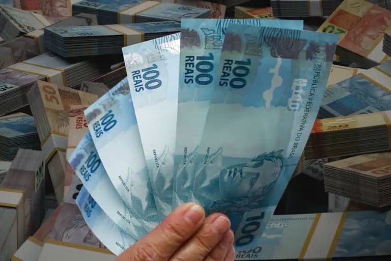Notas de real brasileiro seguradas na mão, representando pagamentos da Caixa Econômica Federal para CPFs com final de 0 a 9.