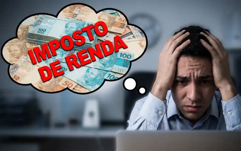 Homem preocupado segurando a cabeça diante do computador pensando no Imposto de Renda com notas de dinheiro ao fundo
