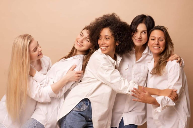 Cinco mulheres sorrindo e abraçadas representam união, diversidade e fortalecimento feminino na data de 8 de março.