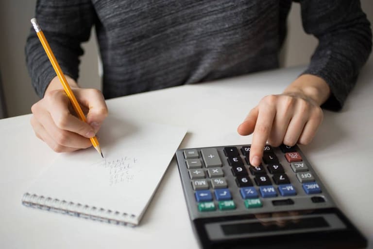 Pessoa usando calculadora e anotando valores para organizar dívidas e aproveitar programa de renegociação bancária.