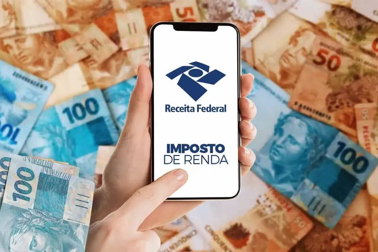 Celular com tela do Imposto de Renda 2026 da Receita Federal sobre notas de real, representando as novas regras e mudanças na declaração