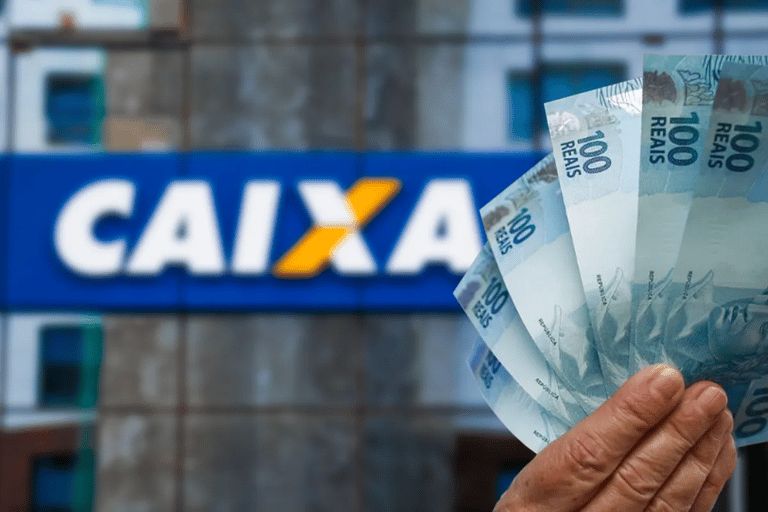 Mão segurando cédulas de reais em frente à fachada da Caixa Econômica Federal