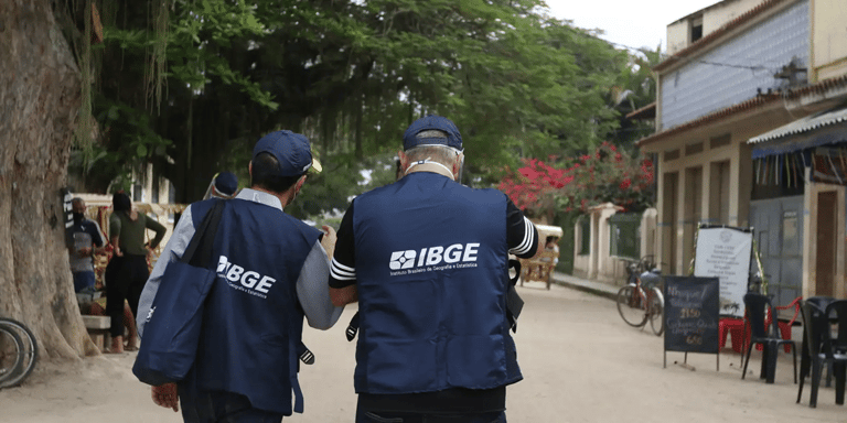 Dois agentes do IBGE uniformizados de costas caminhando em área urbana — concurso IBGE recenseador 27 mil vagas 2026